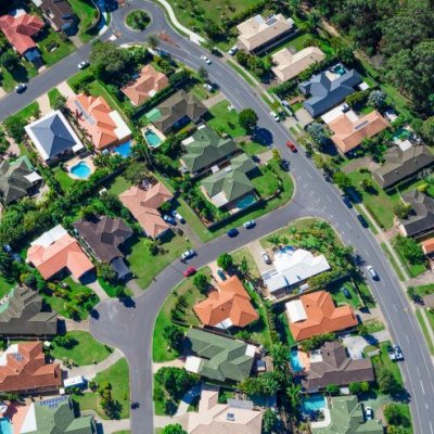 An aerial photo of a typical Australian suburb, showing roads, house rooftops, backyards and swimming pools. 